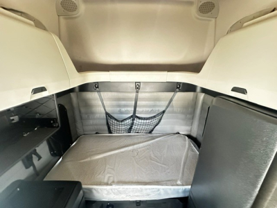 Truck sleeper cab interior showing bed area with gray mattress and storage nets; overhead cab panels and side storage shelves visible.