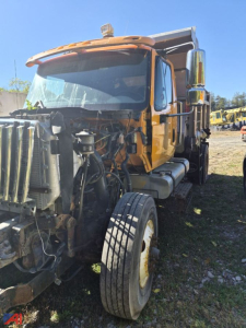 Dump truck with shattered front end showing exposed radiator and engine components; orange cab; International WorkStar 7500 series; VIN plate area not visible; front-left wheel and chassis visible.