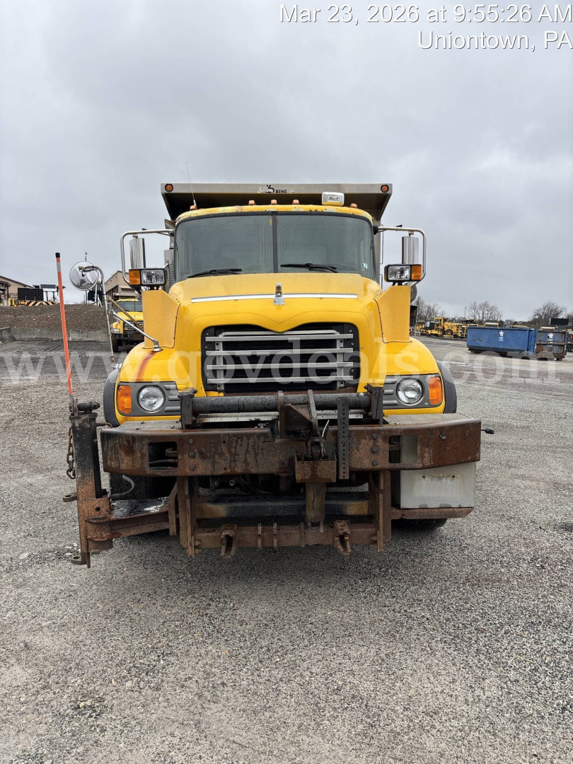 Front view of a yellow 2005 Mack CV713 dump truck showing front grille, headlights, and mounted snow plow with rusted edge.
