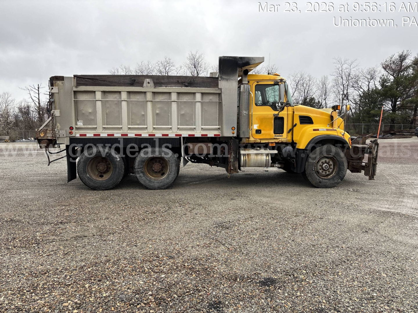 Dump truck with yellow cab and gray dump bed, side view showing Mack CV713 chassis and multiple rear axles.