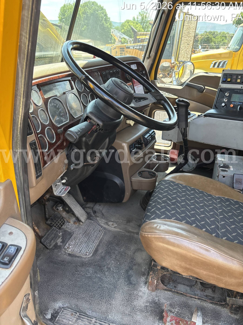 Dump truck cab interior showing steering wheel, dashboard with gauges, driver seat, and pedals.