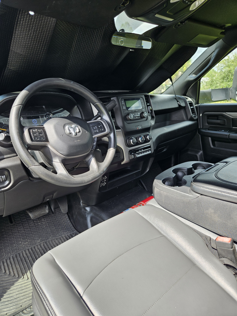 Interior of a 2021 Dodge Ram pickup showing steering wheel with Ram logo, center touch screen, dashboard controls, and front seats.