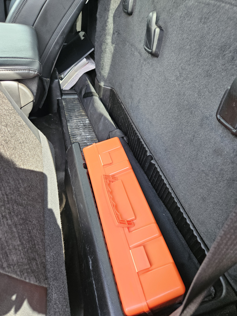 Truck interior showing a bright orange rectangular tool case on the floor near the seat and door panel. No identifiable labels visible beyond that.