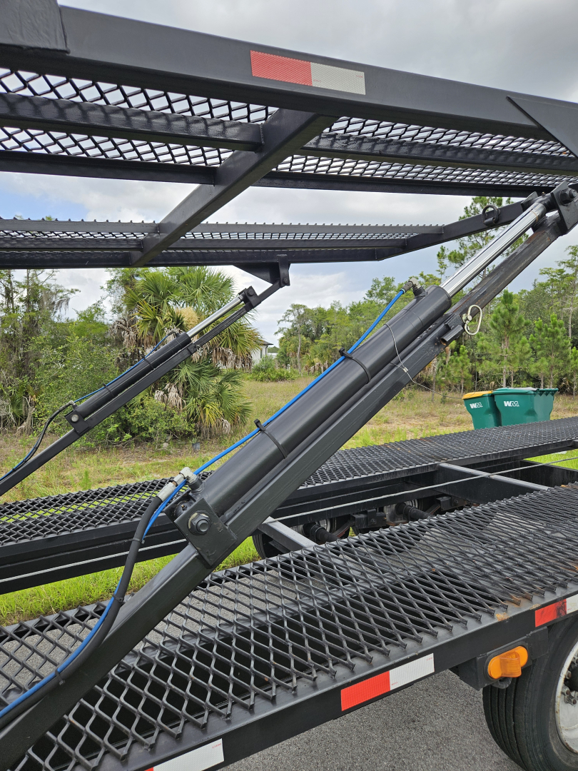 Truck trailer with hydraulic lift cylinders and steel mesh platform showing hydraulic arm and safety rails.