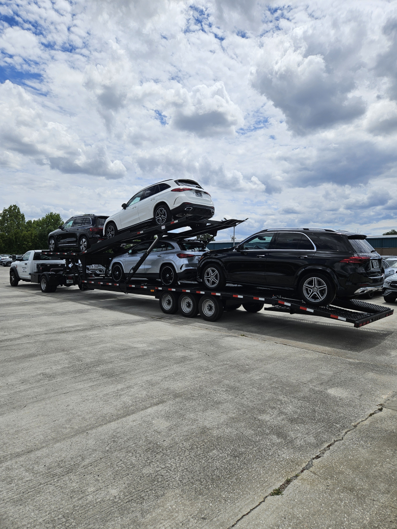 Car carrier trailer with two levels transporting multiple vehicles; white SUV on top, other cars visible on the lower level.