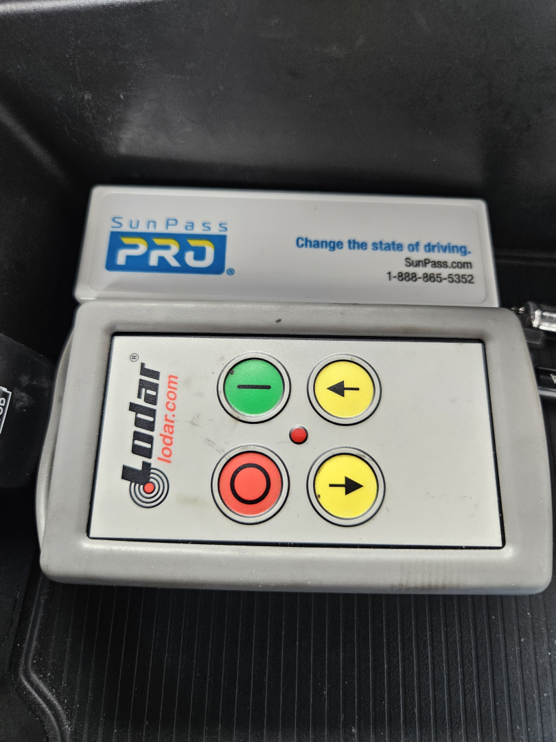 Dodge Ram interior dash area showing Cane SunPass Pro toll transponder with four button keypad: green up, yellow left, red circle, yellow right. Visible text includes 'SunPass PRO', 'change the state of driving', 'SunPass.com', and '1-888-8