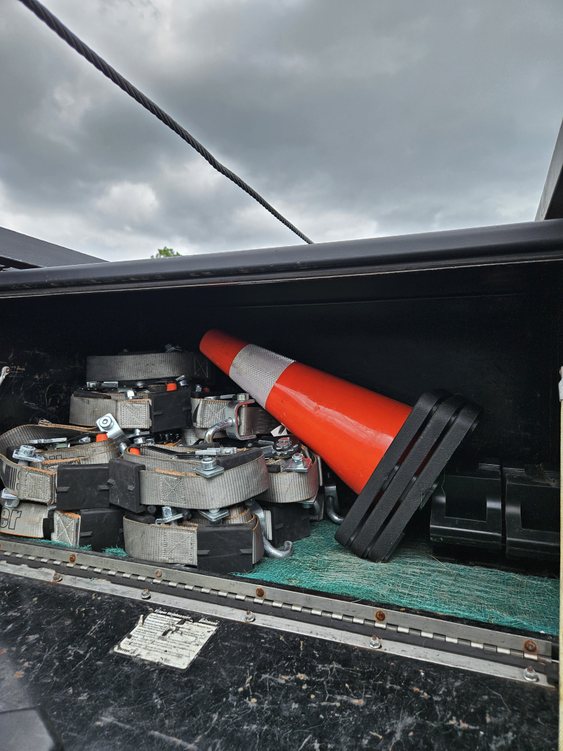 Dodge Ram truck bed with exposed electrical components and a traffic cone placed among wiring harnesses and metal brackets.