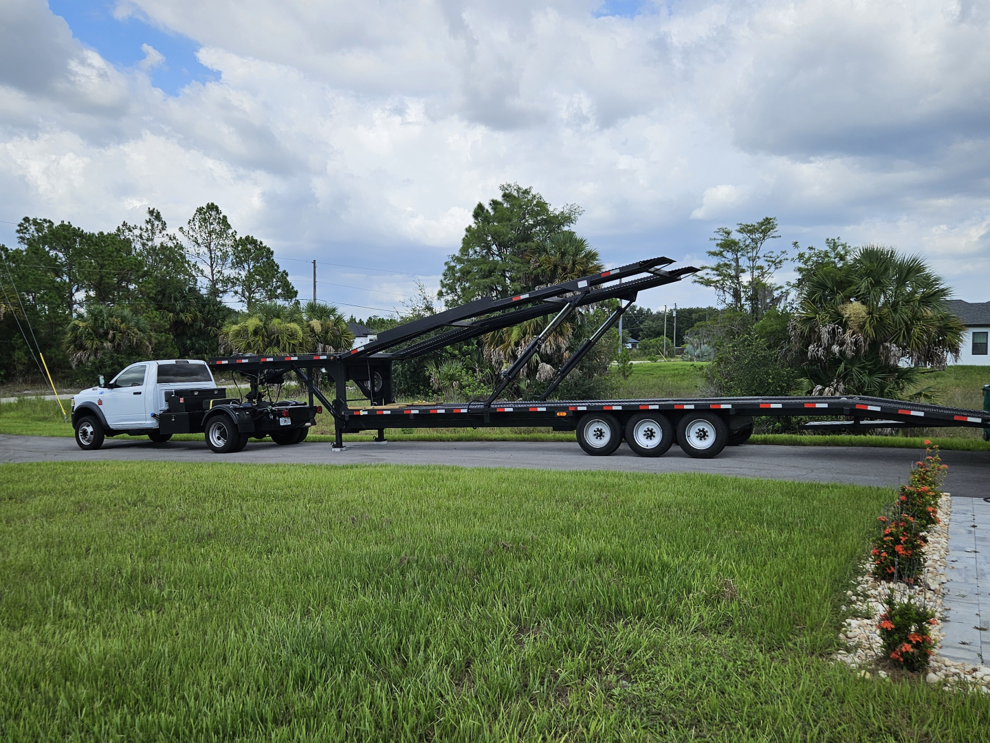Flatbed tow truck with long multi-axle trailer and hydraulic arm, visible in side profile