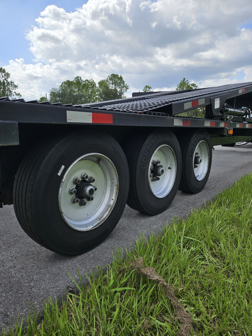 Triple rear axle of a flatbed trailer with wheels and tires visible; no legible markings or labels readable.