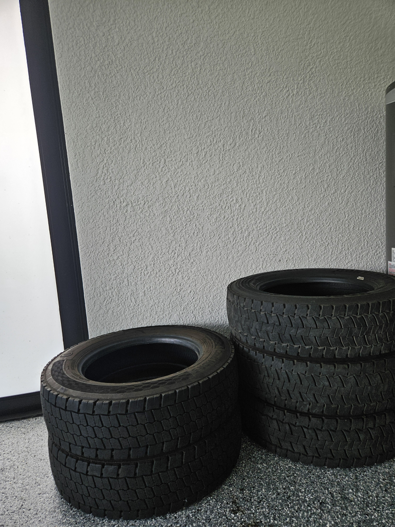 No engine or vehicle components visible; a stack of three tires on a speckled floor against a wall.
