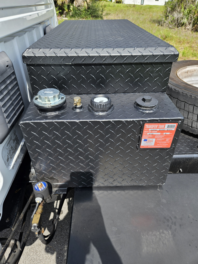 Truck bed toolbox with diamond plate pattern showing two caps and a transfer tank label on the side of a Ram pickup truck.