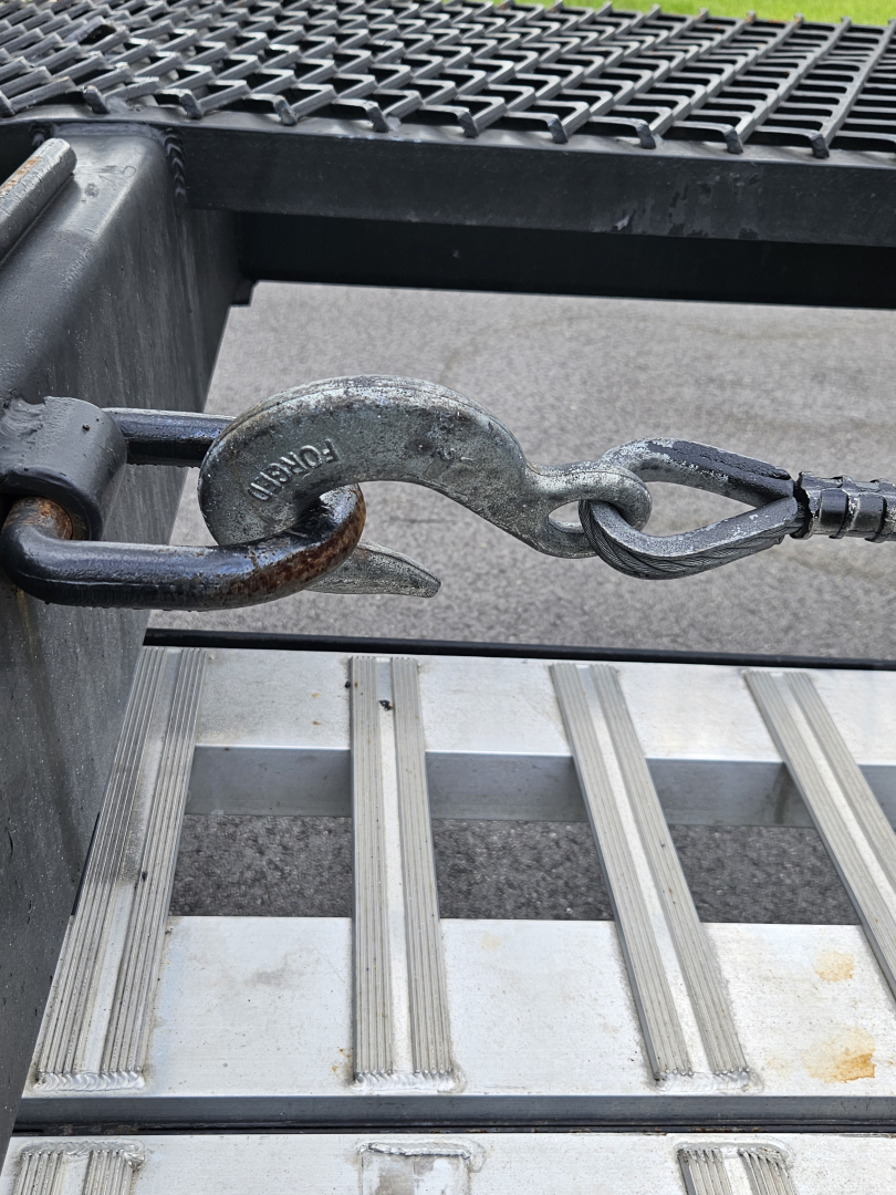 Trailer hitch with lock pin and hook visible on a truck bed step, metal components and textured surface.