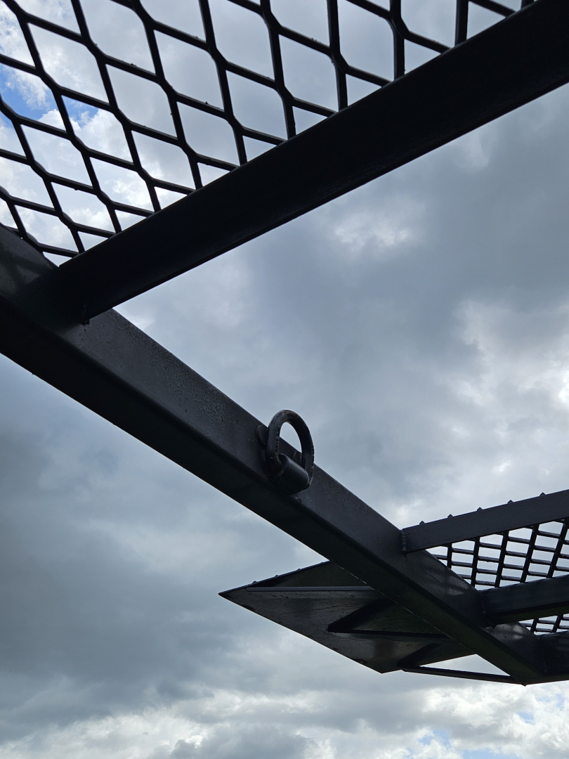 Truck equipment image showing a metal mesh gate and tubular frame, with a cloudy sky in the background.