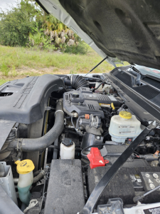 Engine bay of a 2021 Dodge Ram with hood open showing coolant reservoir, battery, and engine components.