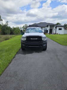 Front view of a white 2021 Dodge Ram pickup truck on a driveway, RAM grille visible, house in background.