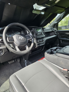 Interior of a 2021 Dodge Ram pickup showing steering wheel with Ram logo, center touch screen, dashboard controls, and front seats.