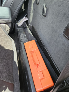 Truck interior showing a bright orange rectangular tool case on the floor near the seat and door panel. No identifiable labels visible beyond that.