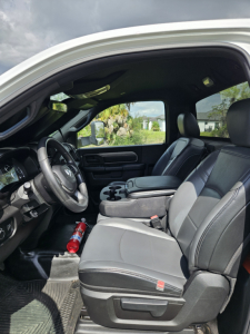 Interior view of a Dodge Ram pickup truck with driver and front passenger seats, steering wheel, center console, and a fire extinguisher in the footwell.