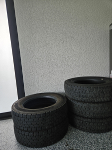 No engine or vehicle components visible; a stack of three tires on a speckled floor against a wall.