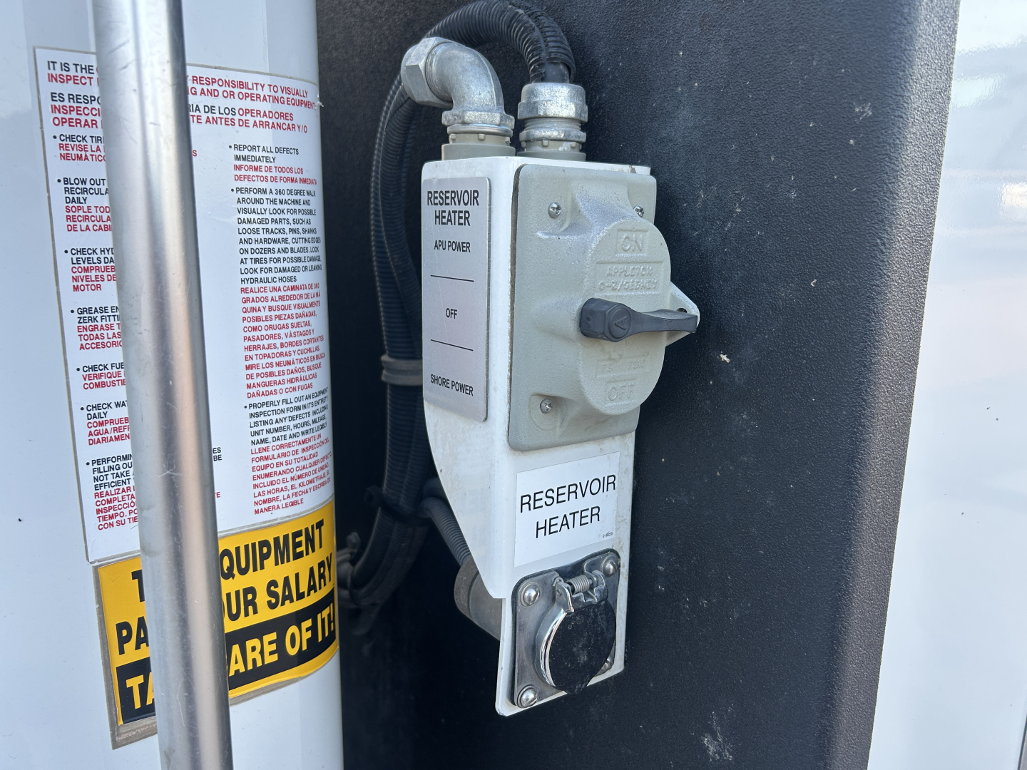 Reservoir heater switch panel and hoses in engine bay of a 2021 Mack MD642 service truck, with warning labels and fluid lines visible.