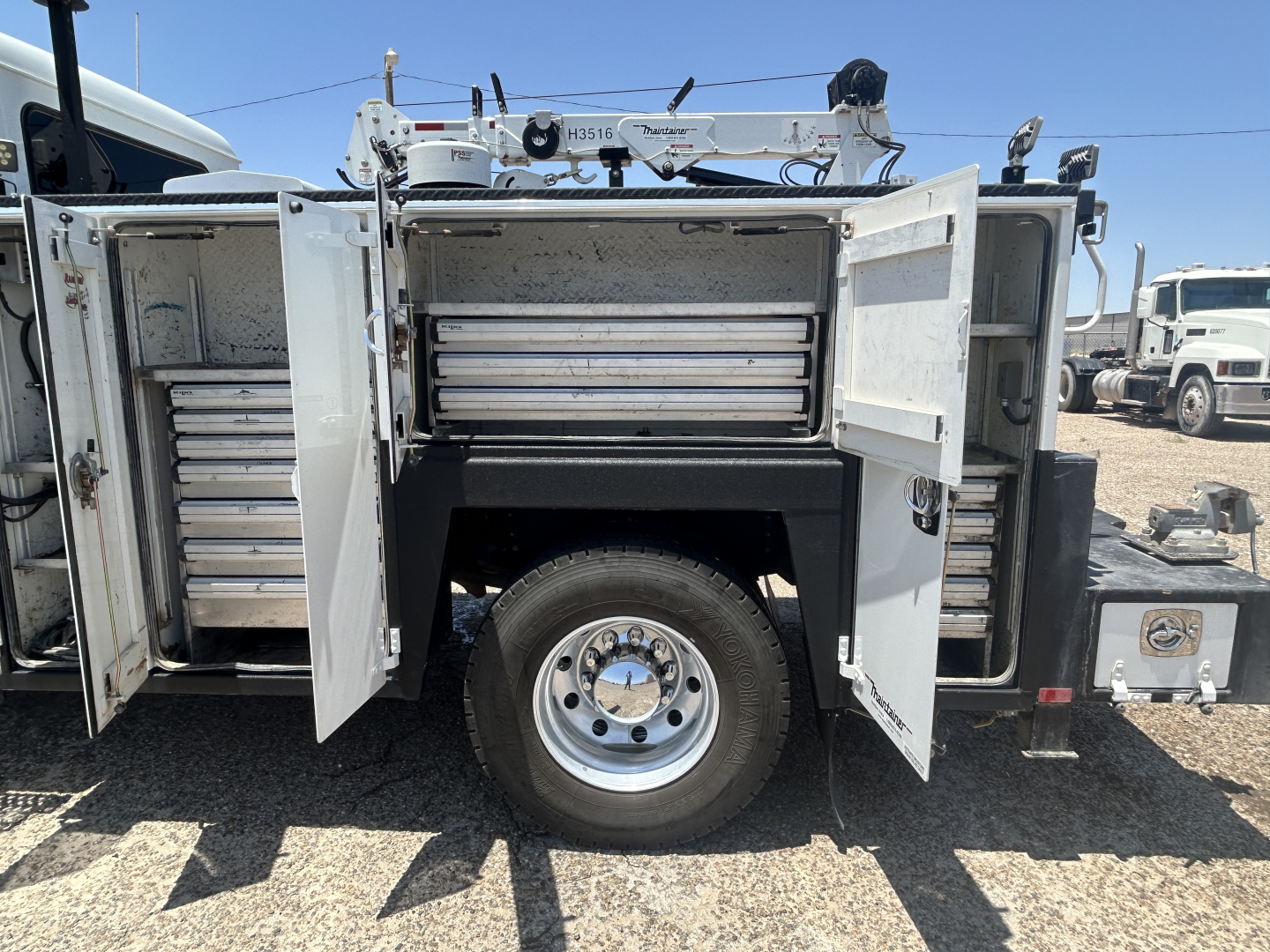 Truck side doors and storage compartments of a 2021 Mack MD642 service truck with multiple toolboxes and a central wheel in view.