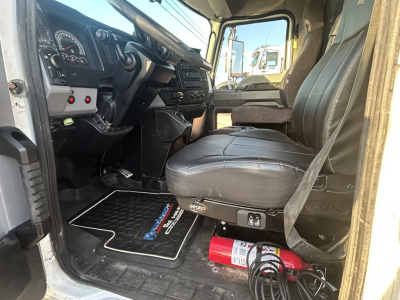 Cab interior of a 2021 Mack MD642 showing steering wheel, dashboard, driver seat, floor mat, and a red fire extinguisher under the seat.