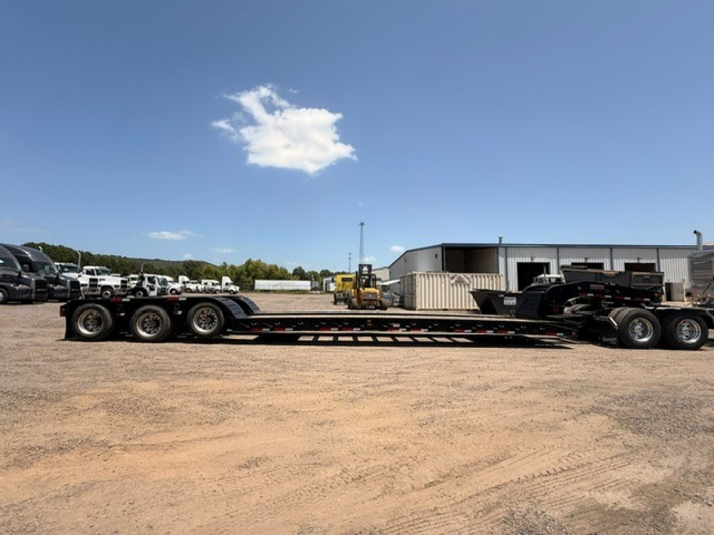  Fontaine MAG55H lowboy trailer in a yard with other equipment and a blue sky.