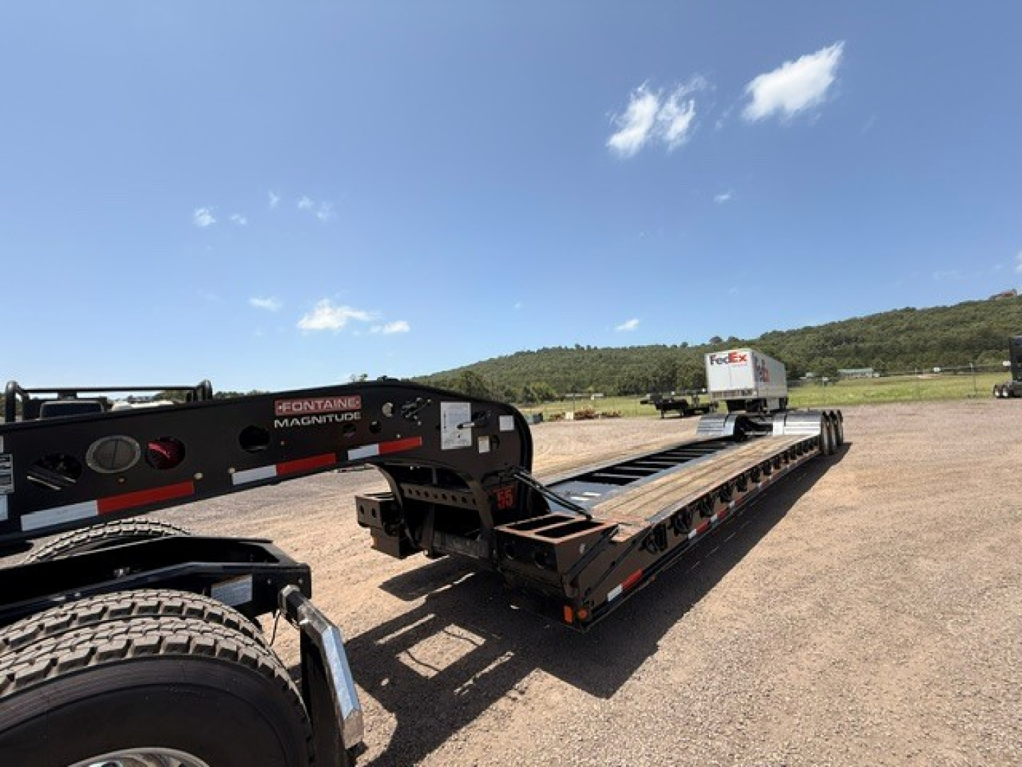  Fontaine MAG55H lowboy trailer viewed from side with loading deck, wheel fender, and a FedEx trailer in distance.