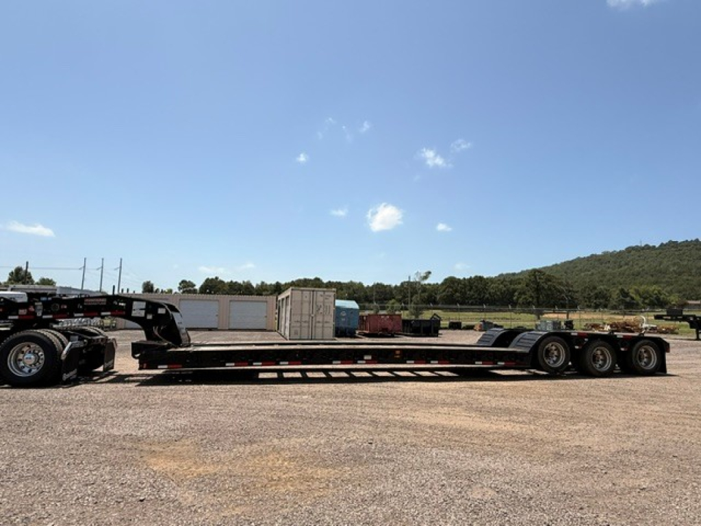 Lowboy trailer with long flatbed and multiple axles; in-field; no visible text on the trailer itself.