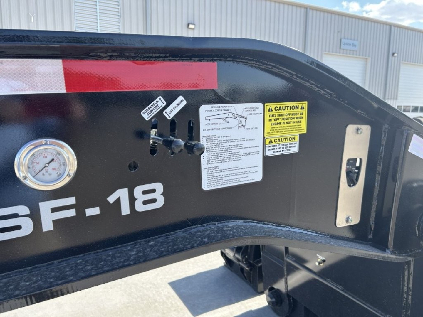 Trailer frame showing LDH label 6F-18, warning decals, gauge, and control levers on black steel surface.