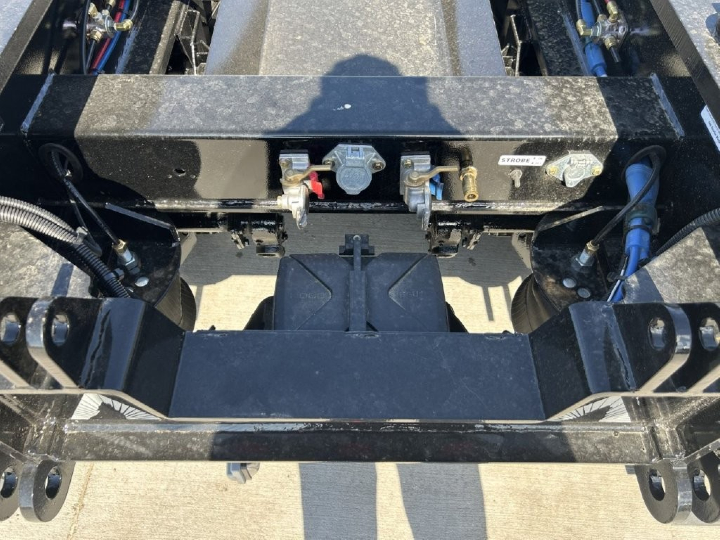Trailer hitch area showing mounting frame and hydraulic connections on a lowboy trailer. Fittings and labels visible.