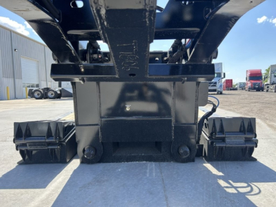Lowboy trailer hitch area showing undercarriage and load bearing beam with metal spiked stabilizers and wheel hubs.