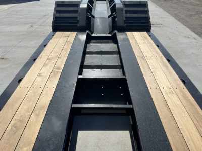 Lowboy trailer bed with wooden deck planks and a central black steel spine; top view shows front gooseneck area and side tie-down channels.