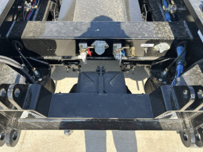 Trailer hitch area showing mounting frame and hydraulic connections on a lowboy trailer. Fittings and labels visible.