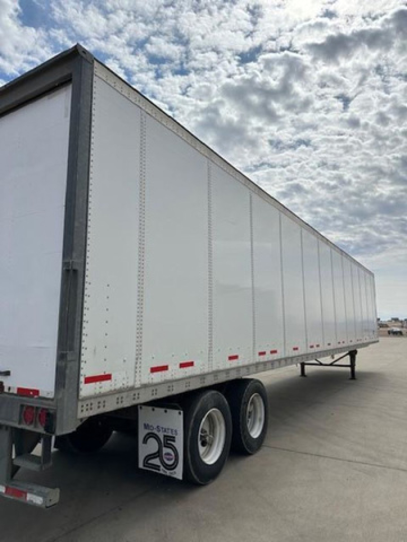 Trailer side view showing a white Wabash van trailer with dual rear axles and red reflective markers along the lower edge.