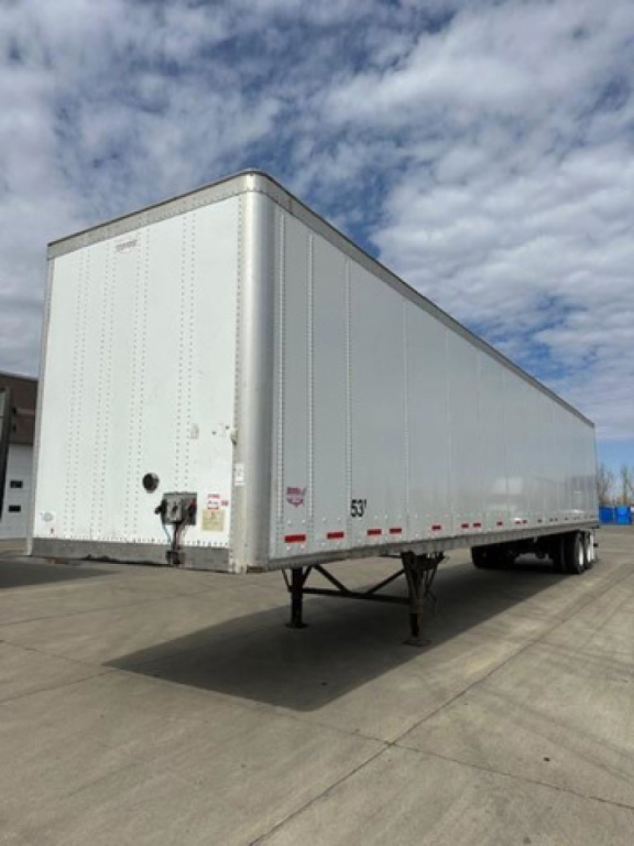 Trailer side view showing a white 2014 Wabash van trailer, closed box with nose hitch, supported by landing gear, parked on pavement.