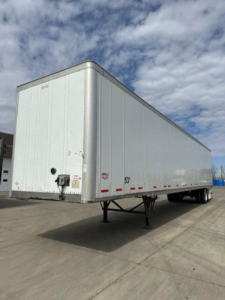 Trailer side view showing a white 2014 Wabash van trailer, closed box with nose hitch, supported by landing gear, parked on pavement.