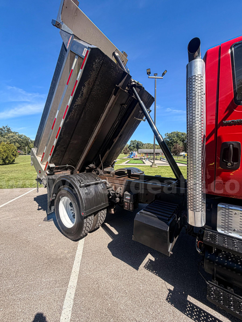 Dump truck bed with raised hydraulic dump on a red International 7400, side view showing tilted cargo bed and dual rear wheels.