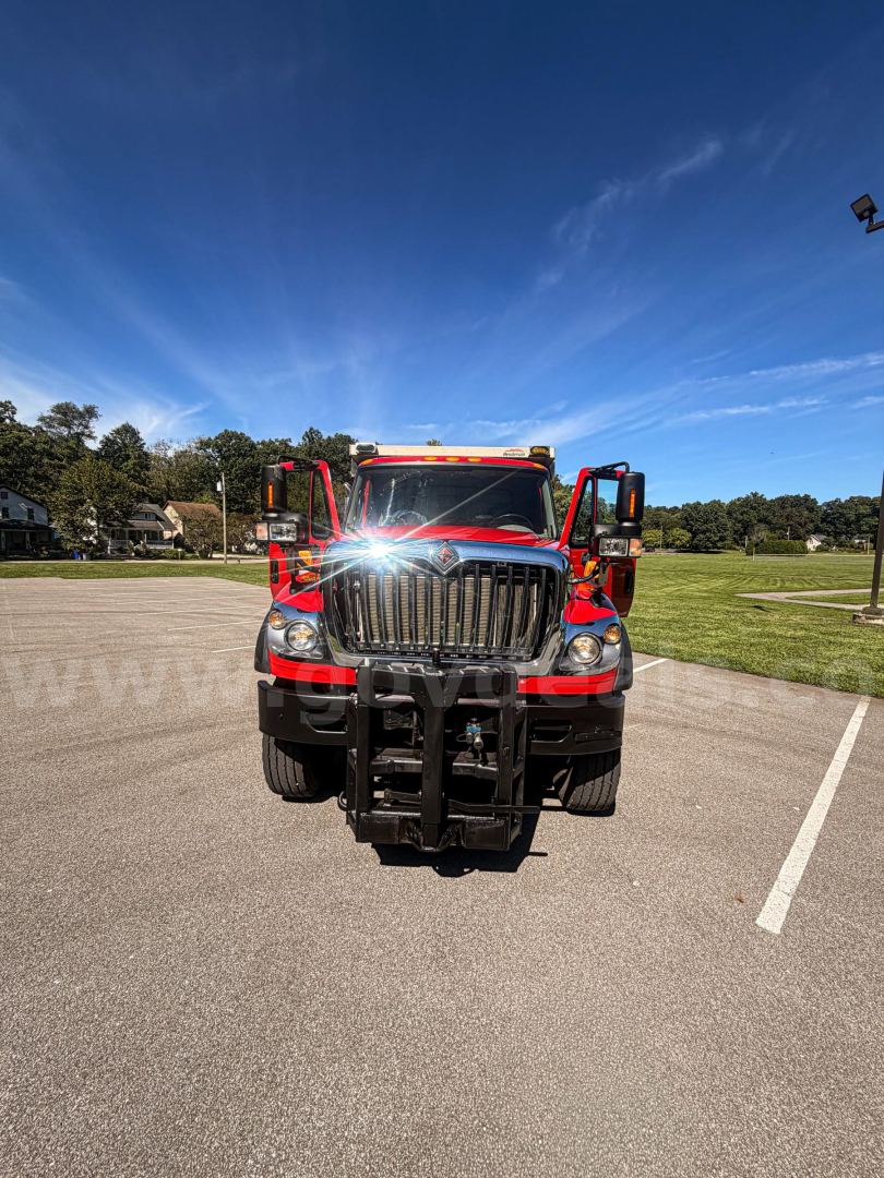 Truck front view of a red 2014 International 7400 with plow mount in foreground, cab doors open, clear sky.
