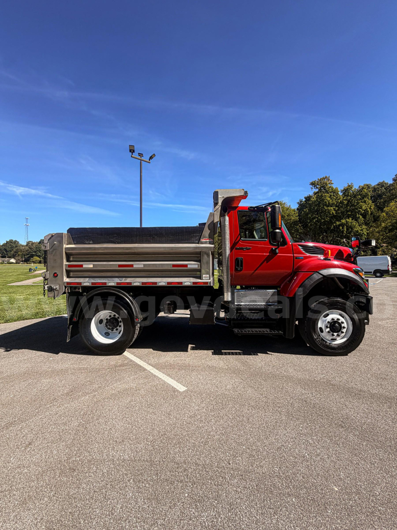 International 7400 dump truck side view in a parking lot with red cab and metallic bed, plow equipment not visible.