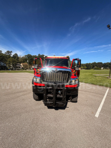 Truck front view of a red 2014 International 7400 with plow mount in foreground, cab doors open, clear sky.