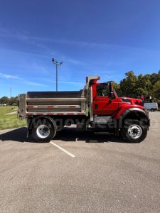International 7400 dump truck side view in a parking lot with red cab and metallic bed, plow equipment not visible.