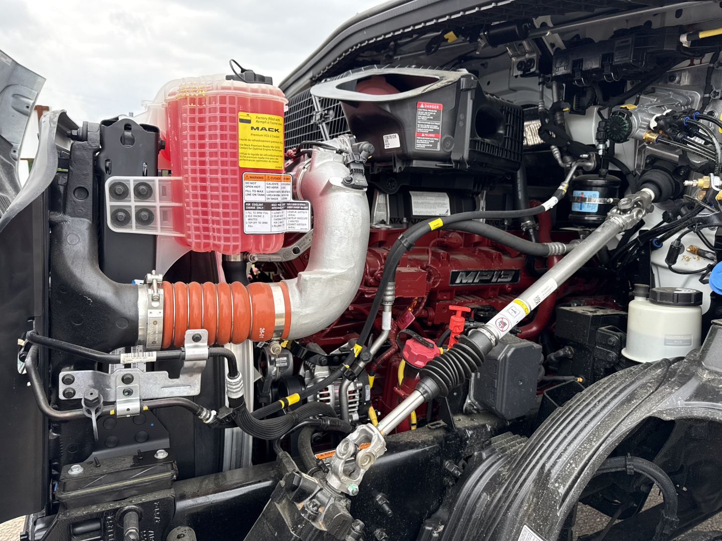 Mack AN64T engine bay showing air intake, coolant reservoir, hoses, and battery; red air filter housing and components visible.