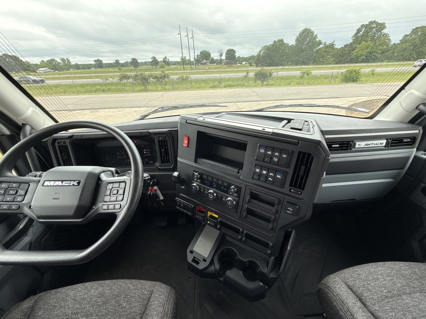 Interior view of a 2027 Mack AN64T conventional daycab cab interior; steering wheel with Mack logo, dashboard with control panels, center console, gear shifter, and driver and passenger seats.