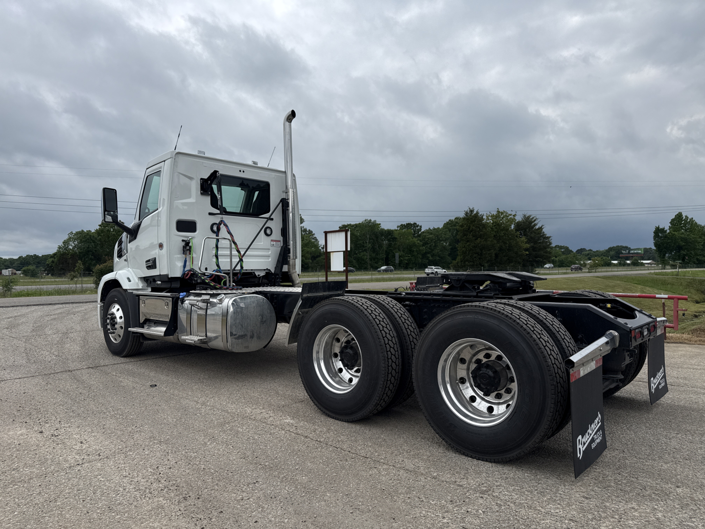 Truck chassis and cab of a 2027 Mack AN64T with dual rear axles, white cab, side fuel tank, exhaust stack, and OEM branding on mudflaps.