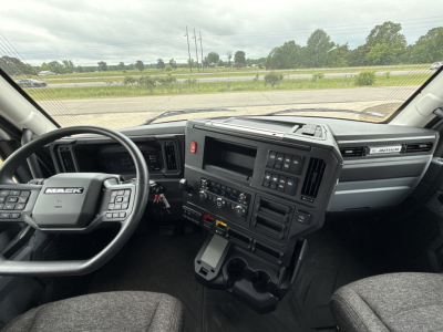 Interior view of a 2027 Mack AN64T conventional daycab cab interior; steering wheel with Mack logo, dashboard with control panels, center console, gear shifter, and driver and passenger seats.