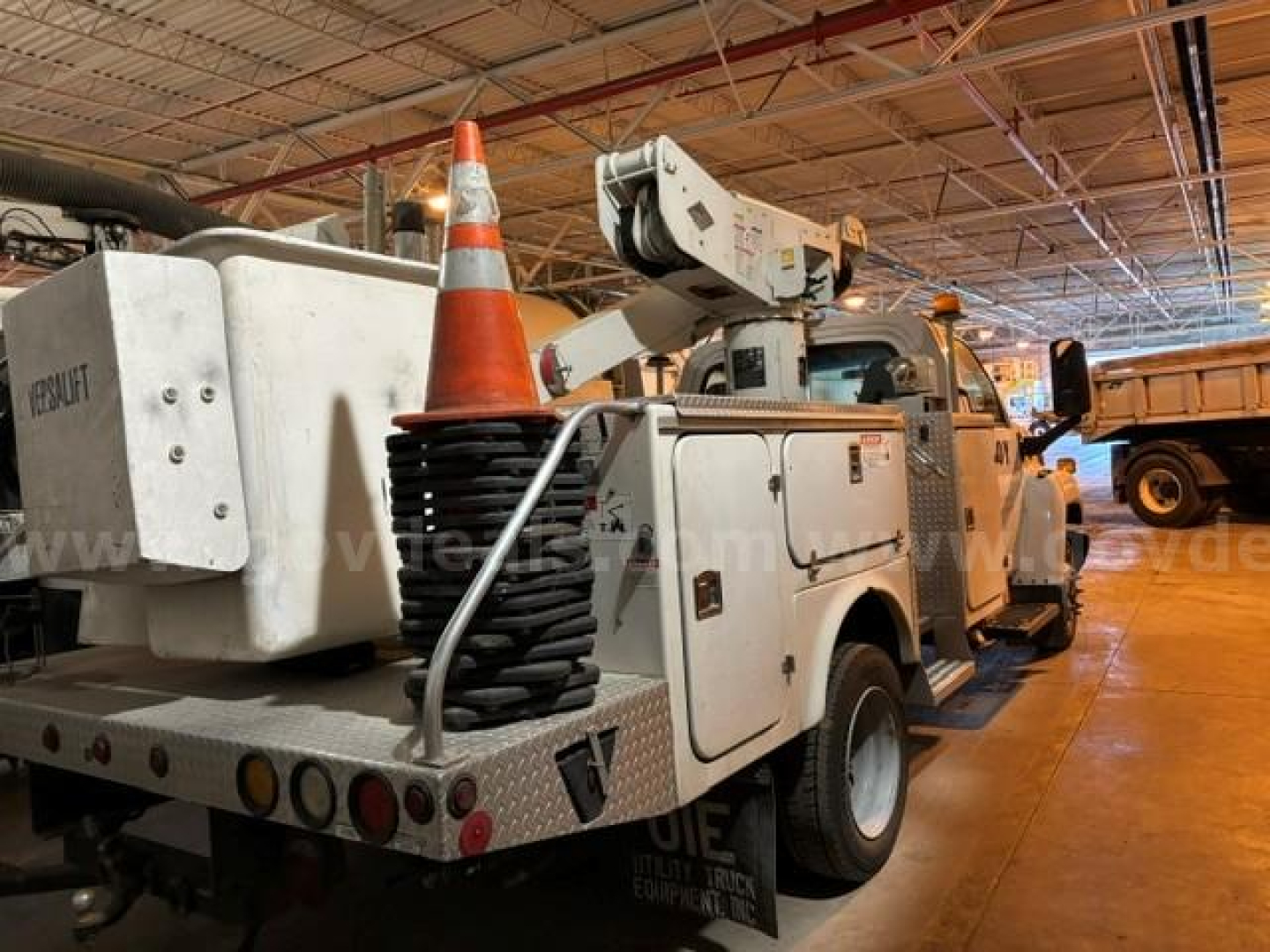 Truck utility bed with hydraulic crane inside a warehouse showing a traffic cone and work light.