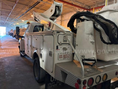 Truck utility body with bucket lift and rear platform showing utility controls and a white cab in an indoor lot.