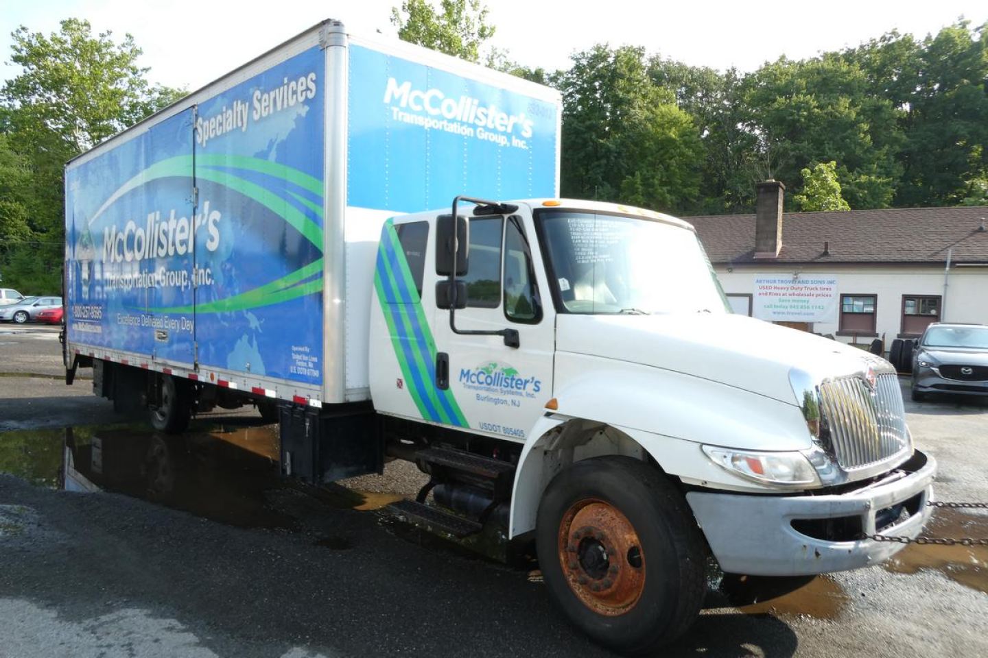 Box truck showing McCollister's Specialty Services logo and blue cargo box, International truck with white cab and branded graphics.