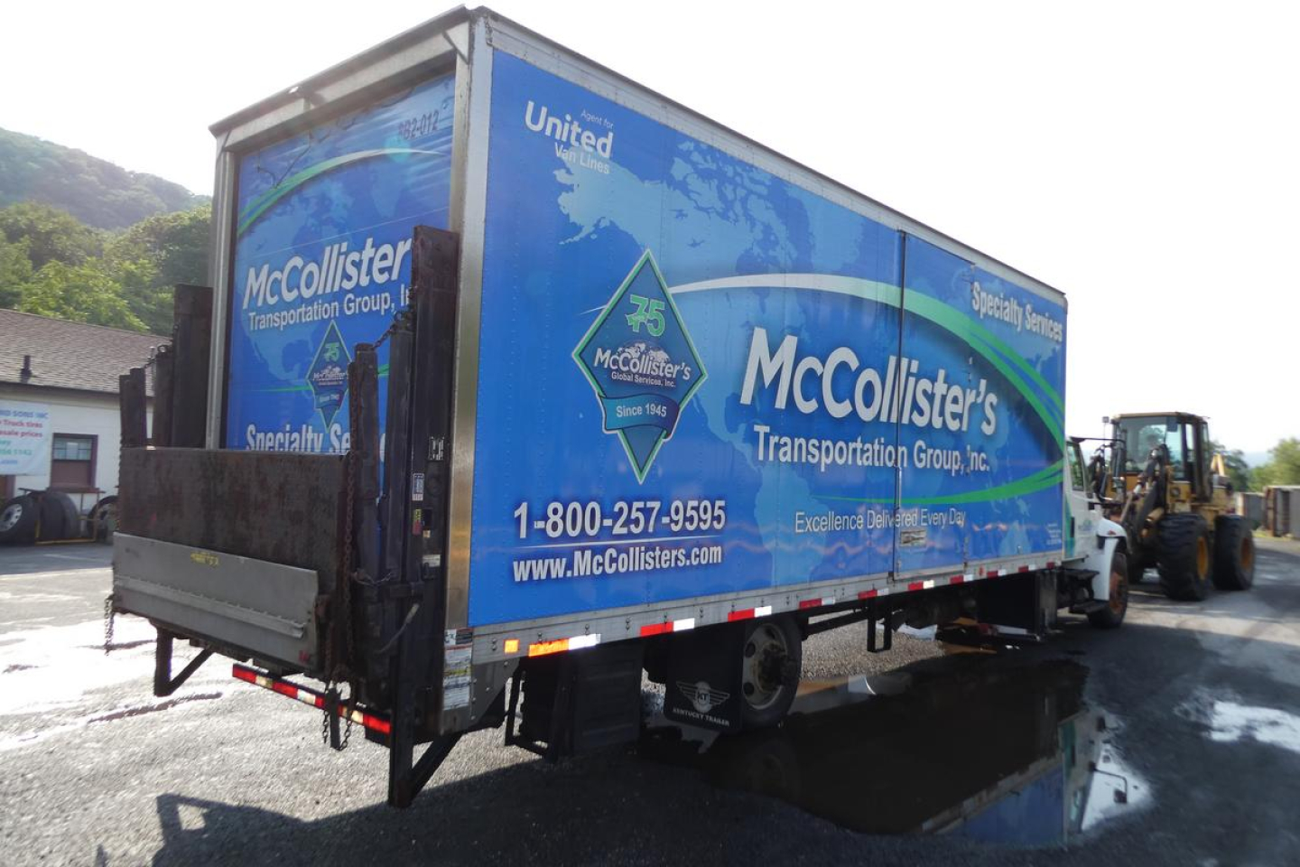 Box truck trailer with McCollister's Transportation Group logo in blue livery and United logo, tractor unit on right, rear loading ramp visible.